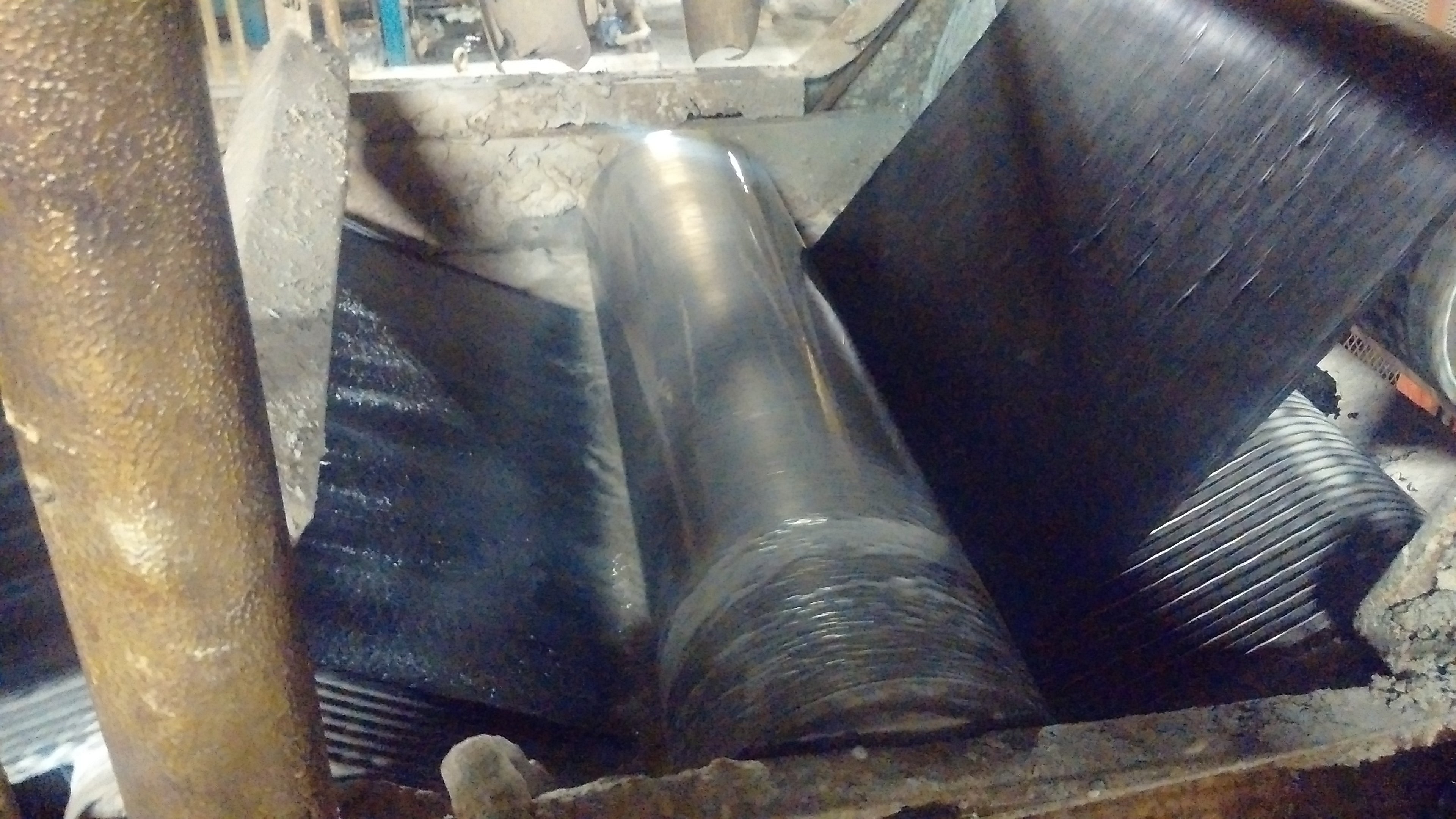 Rolls of black rubber sheeting on a metal surface with industrial equipment in the background.