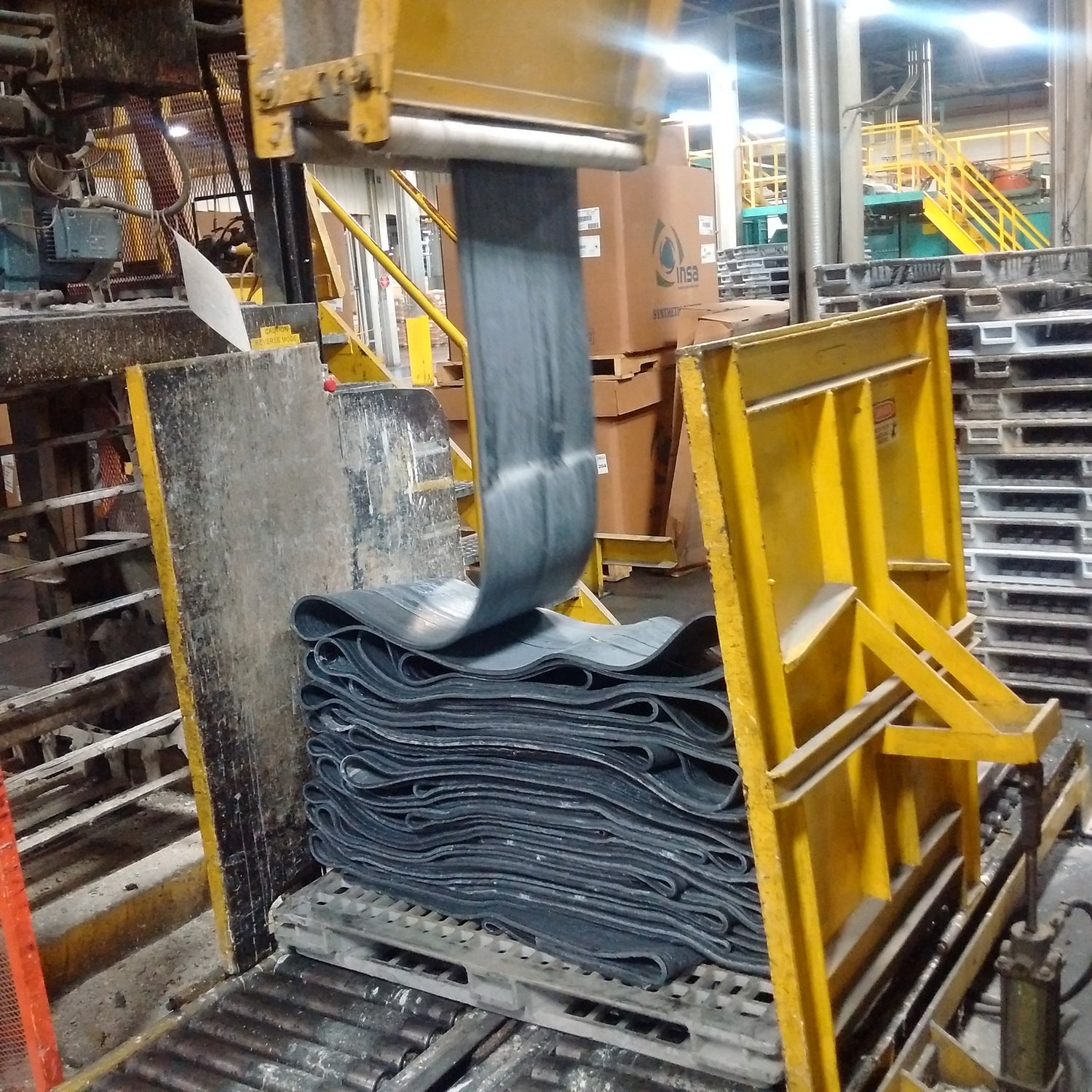 Stack of blue rubber sheets being lifted by a yellow forklift in an industrial setting.