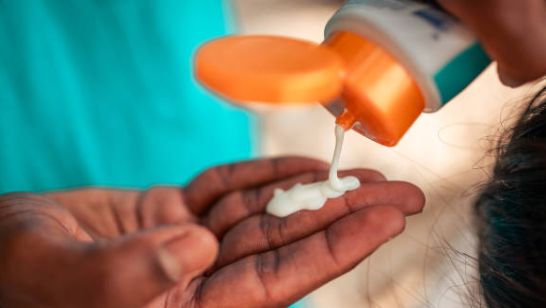 Person applying white cream from a tube onto their hand against a blurred background