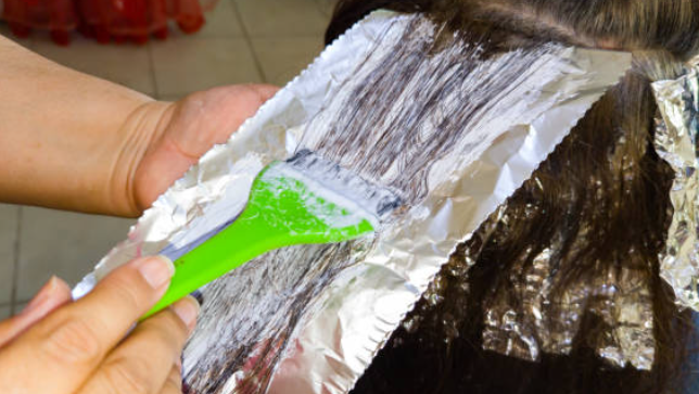 Person applying a white substance to a piece of tinfoil with a green spatula.