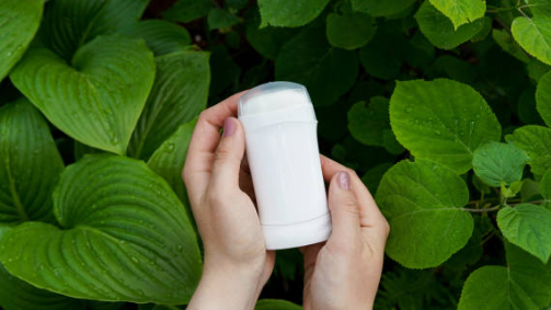 Person holding a white cylindrical container against a green leafy background