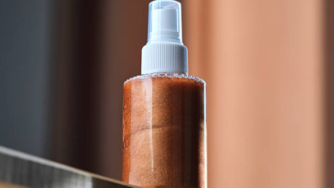 Wooden spray bottle with a clear spray nozzle on a reflective surface.
