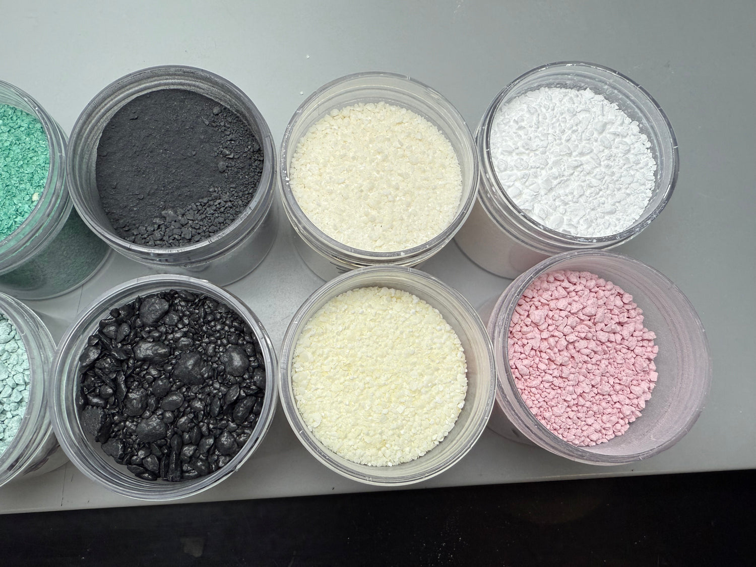 Assorted colored powders in small plastic containers on a gray surface
