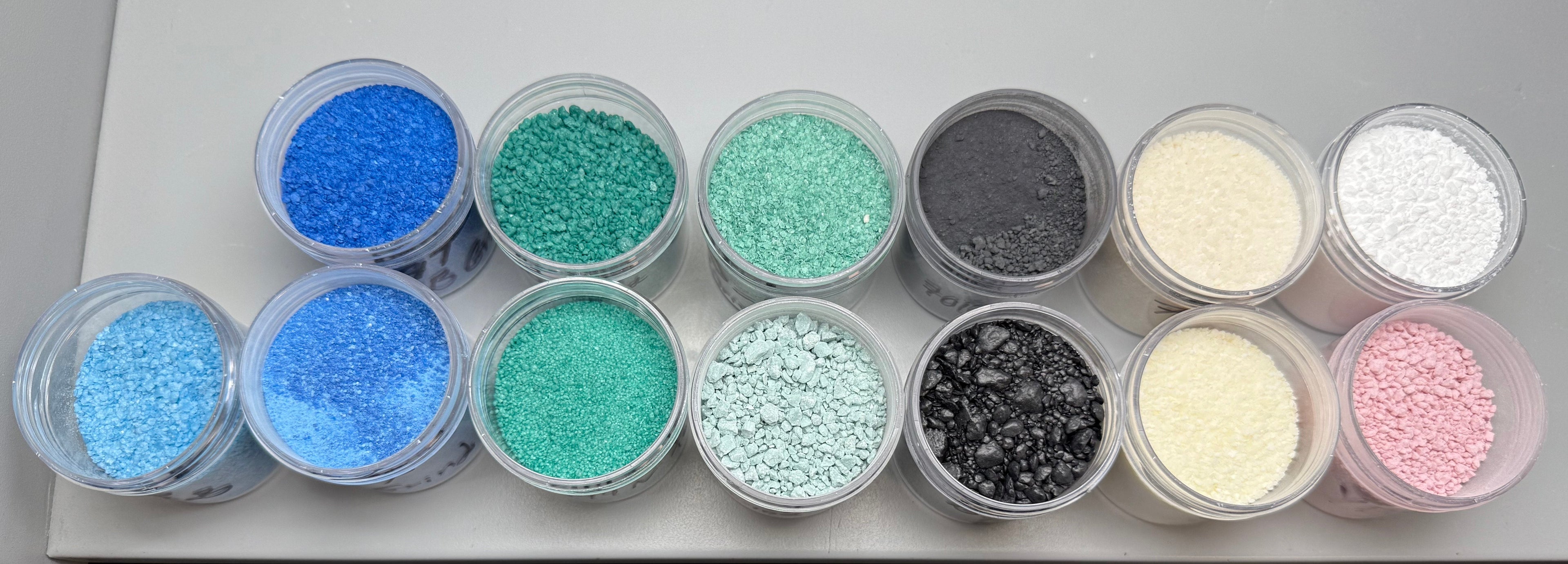 Assorted colored glitter in small round containers on a white surface.