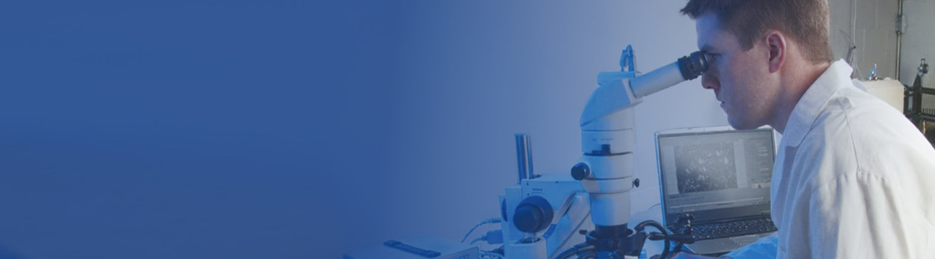 Person using a microscope with a laptop in a laboratory setting