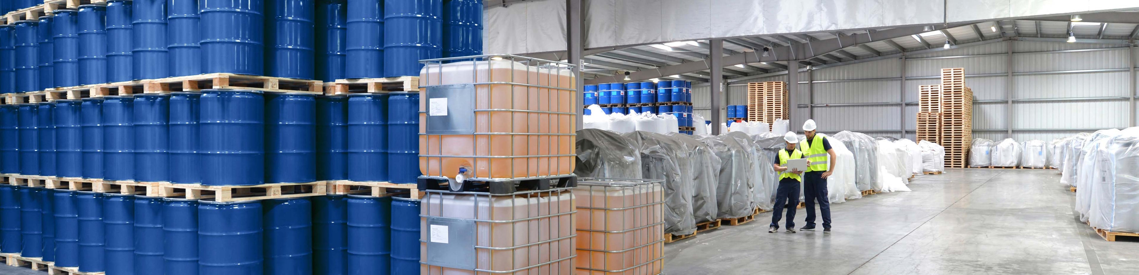 Warehouse with stacks of blue barrels, cardboard boxes, and workers.