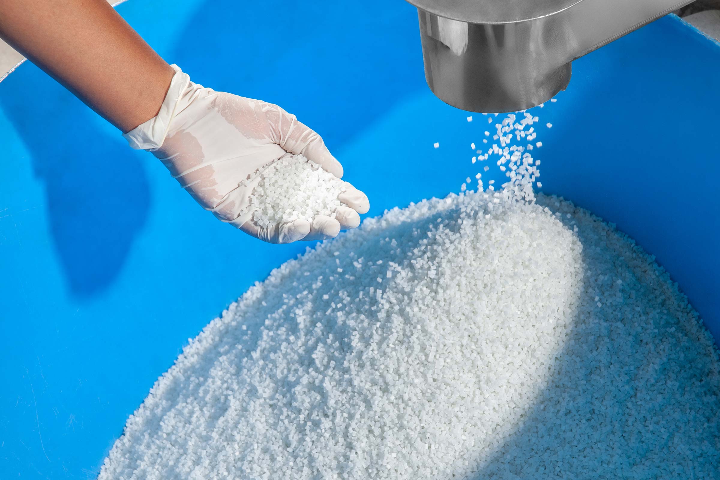 Person wearing gloves pouring a white powdery substance into a blue container.
