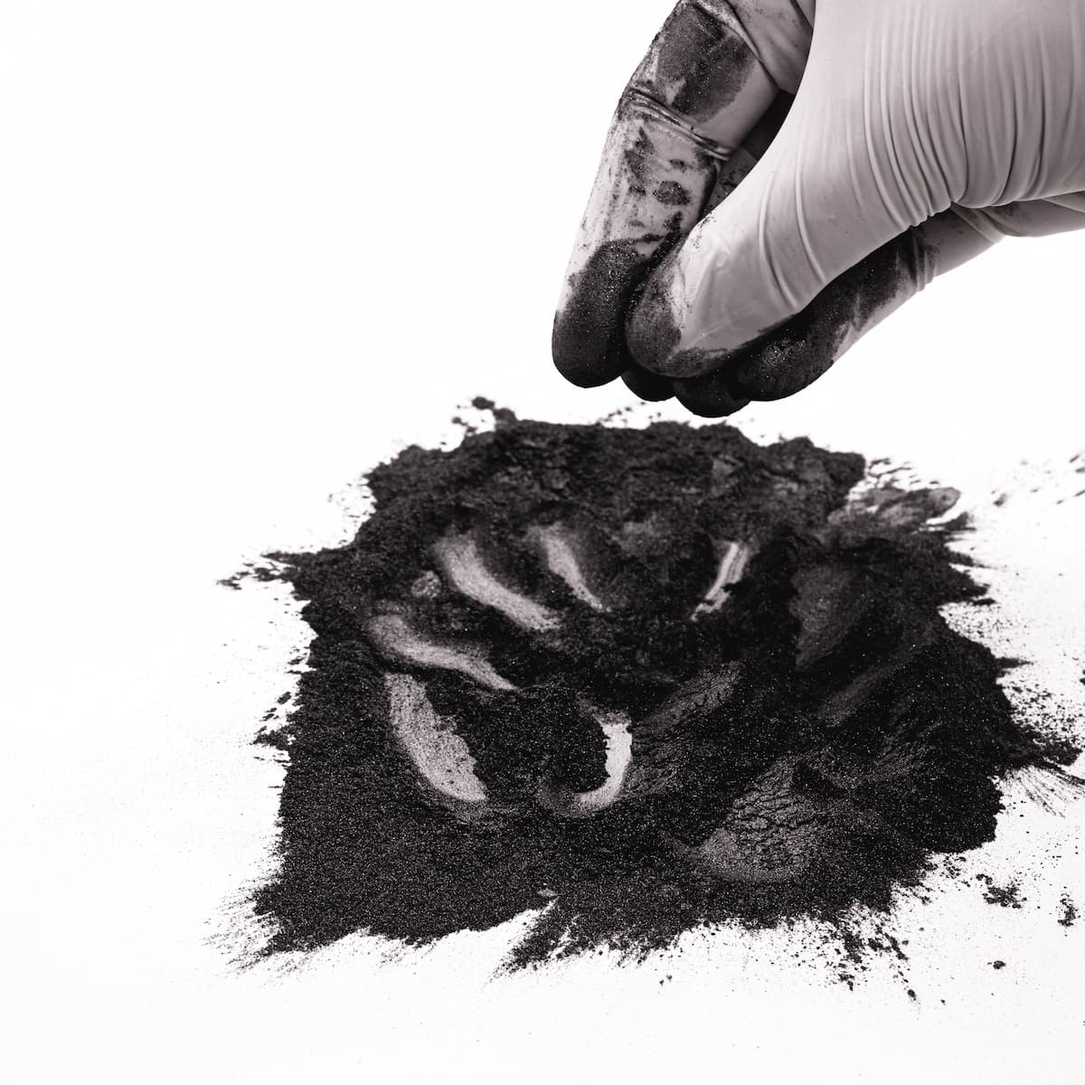 Hand wearing a glove holding a small pile of dark powder on a white background
