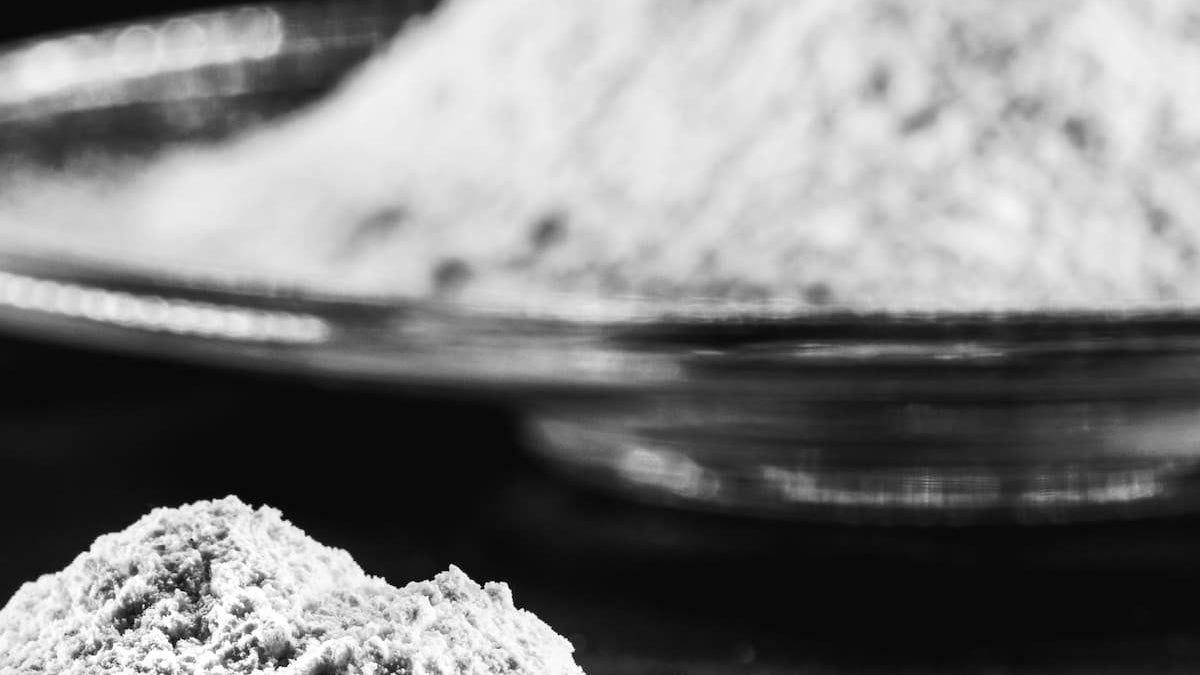 Close-up of a glass bowl with a pile of gray powder on a dark background