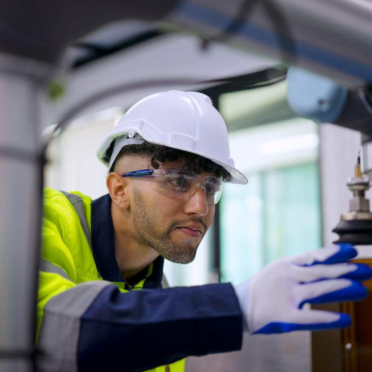 Person wearing a hard hat and safety glasses working on machinery.