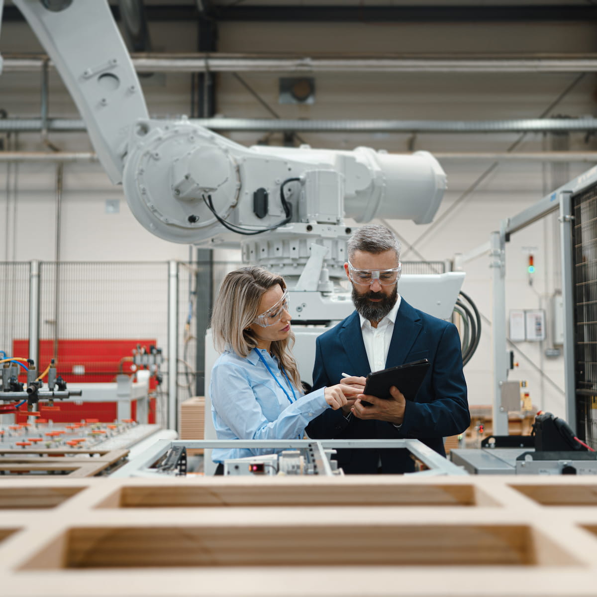 Two professionals interacting with a robot arm in an industrial setting