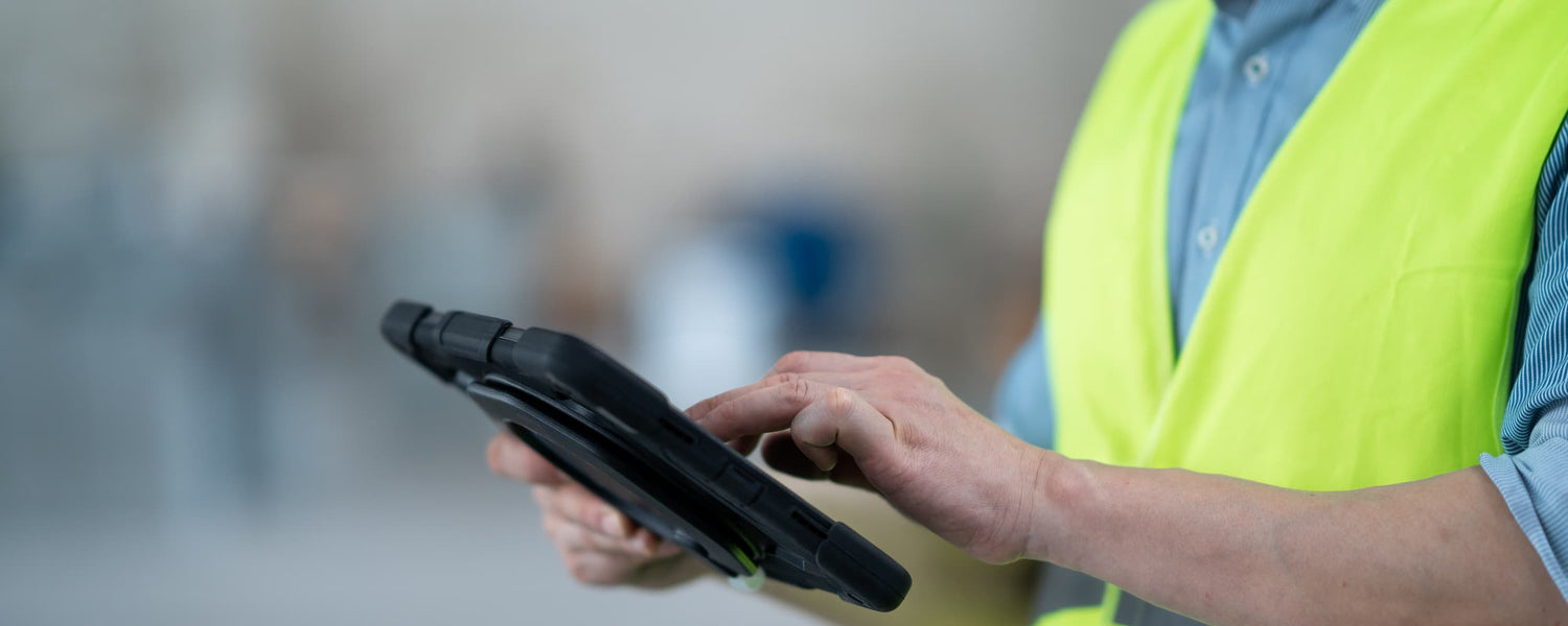 Person wearing a high-visibility vest holding a tablet device.