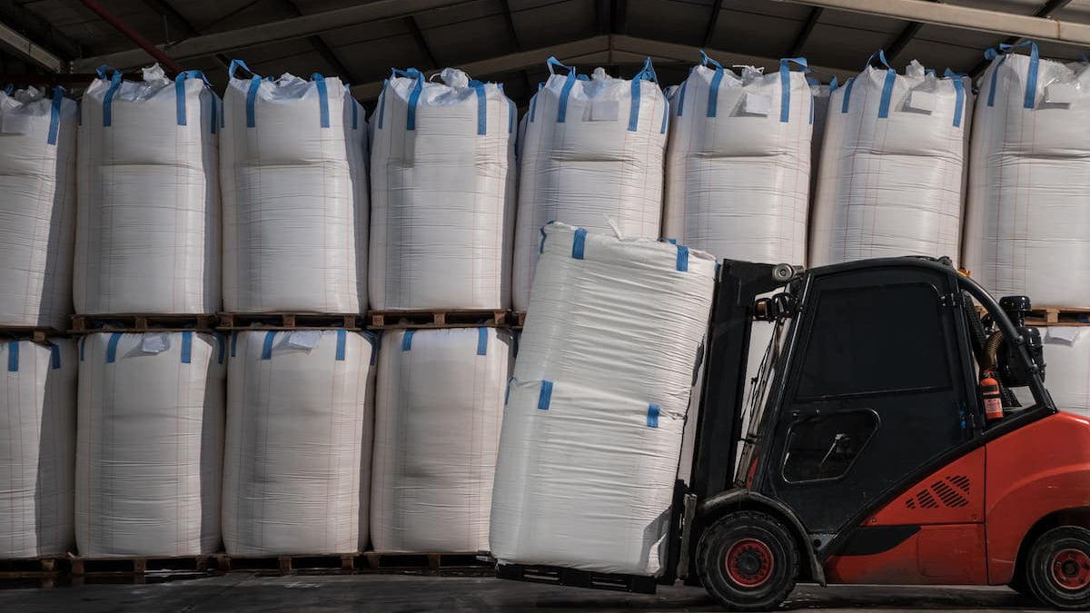 Forklift moving large white bags in a warehouse setting