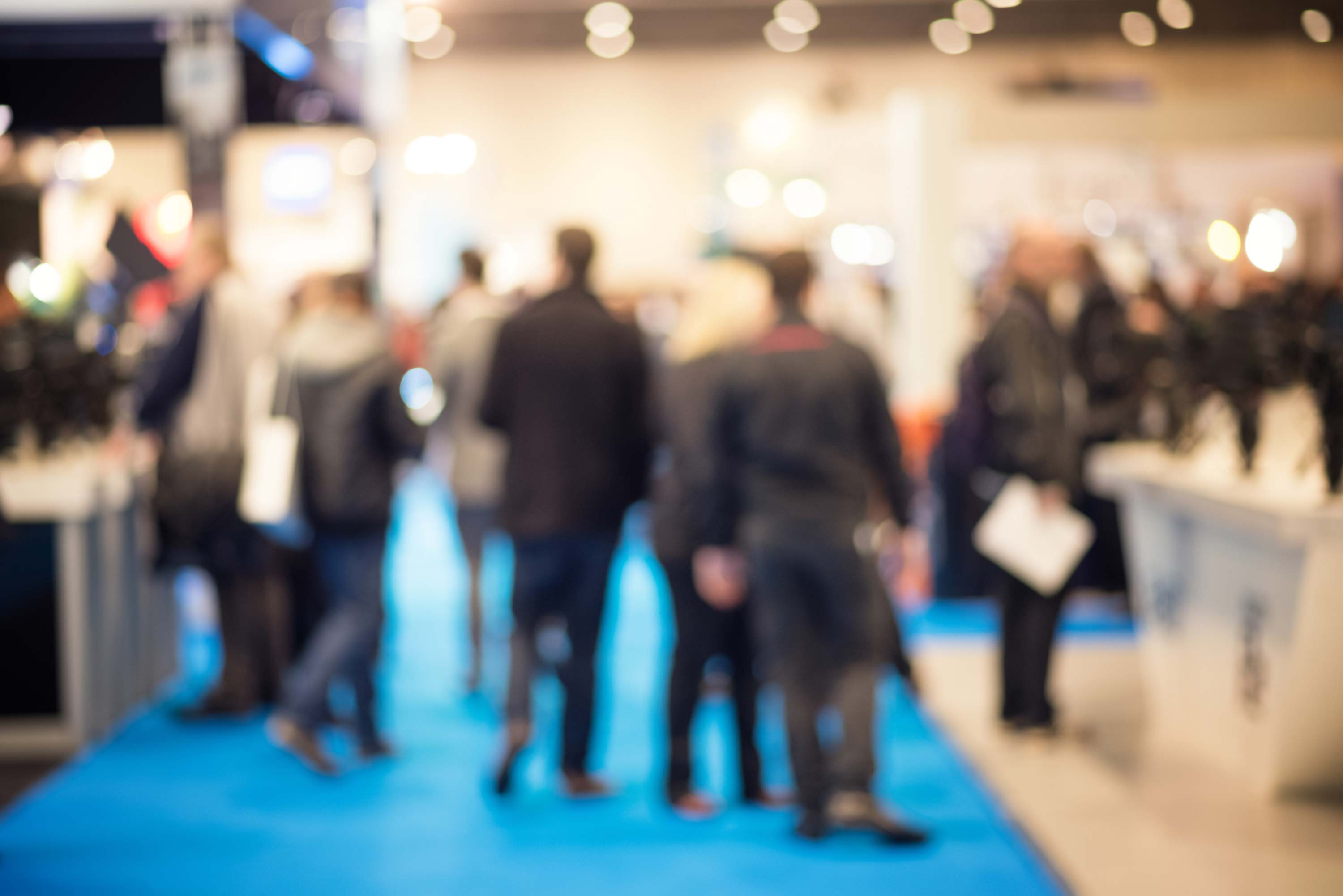 Blurred image of people walking on a blue carpet at an event