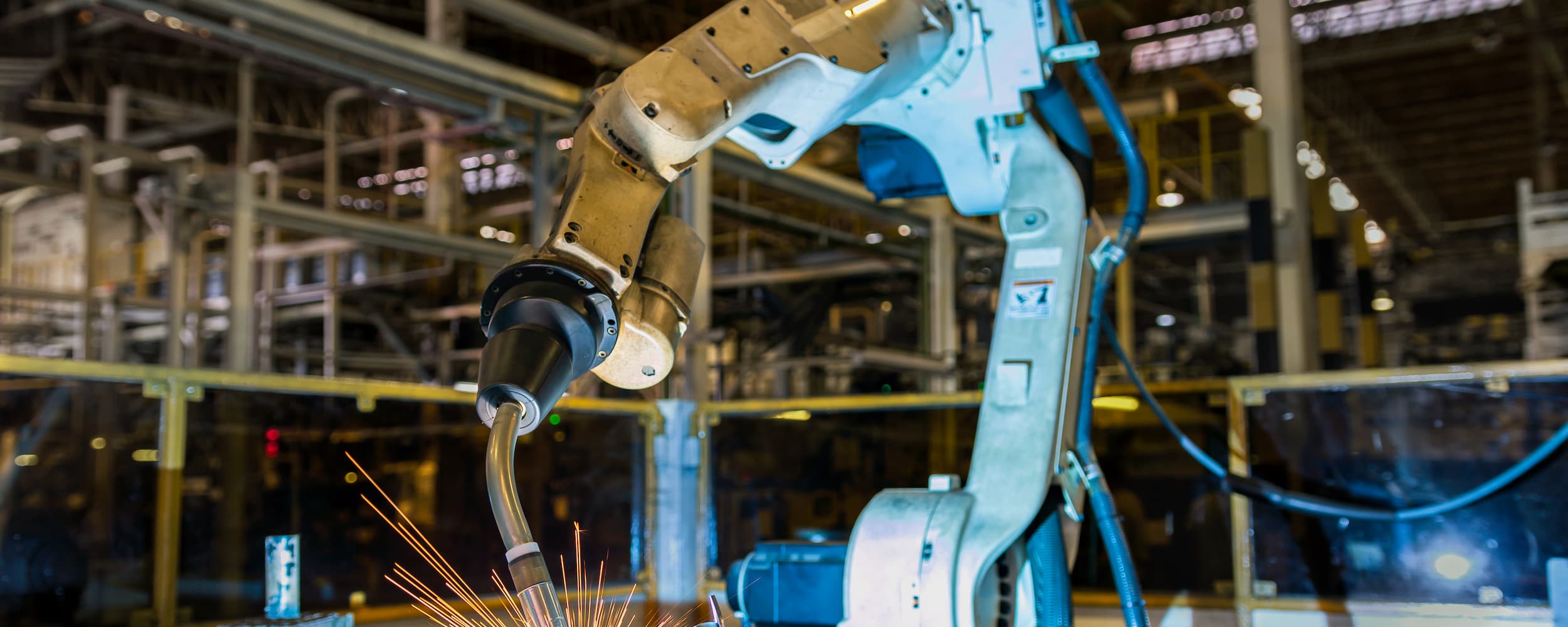 Robotic arm in an industrial setting with sparks, likely from welding.