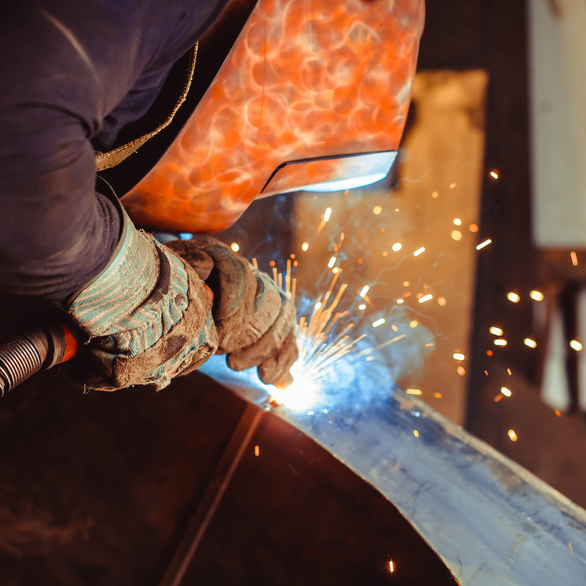 Person welding metal with sparks flying, wearing protective gloves.