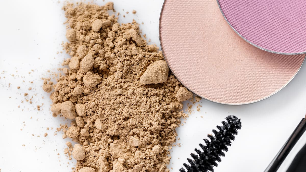 Makeup products including a compact powder, blush, and mascara on a white background