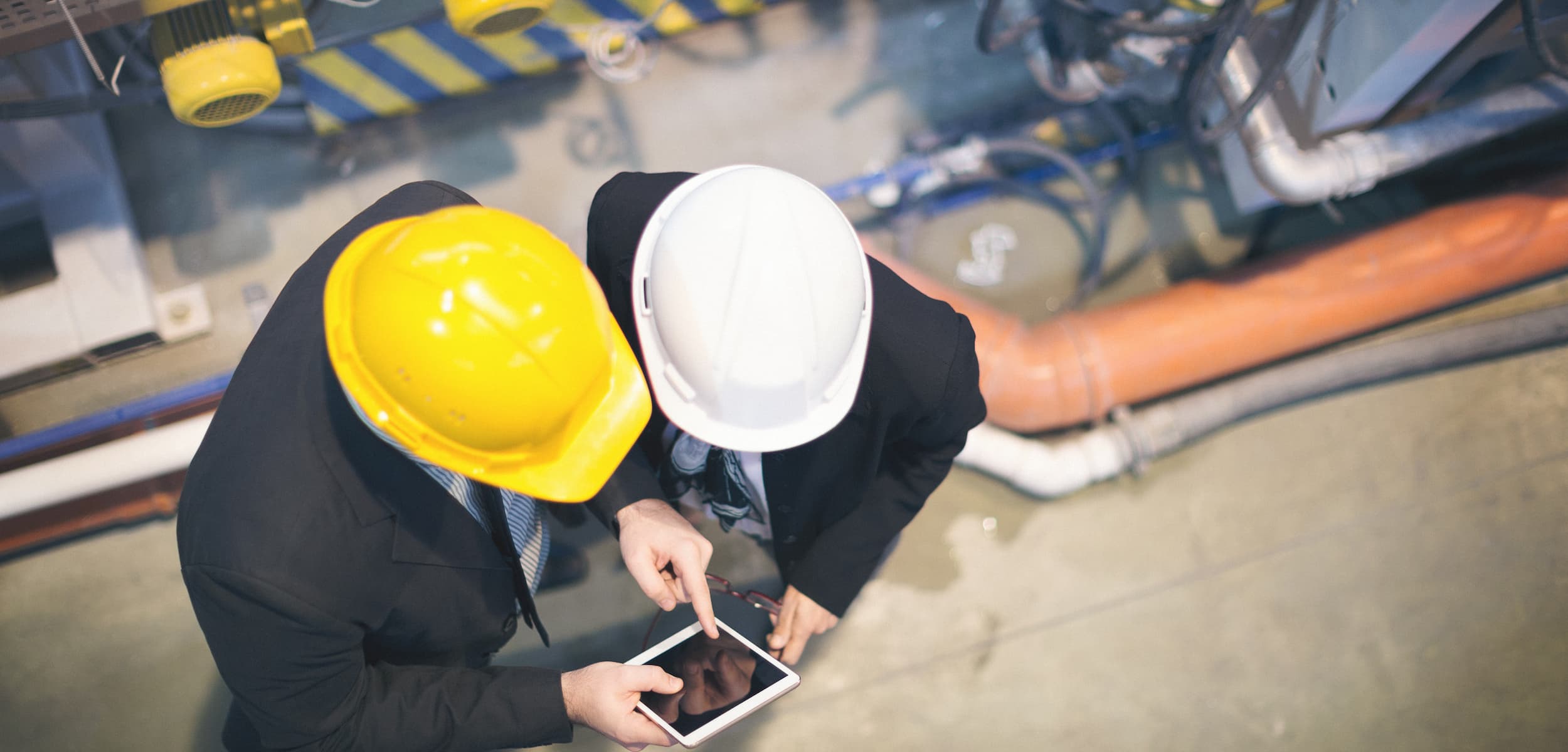 Two individuals wearing hard hats looking at a smartphone in an industrial setting.