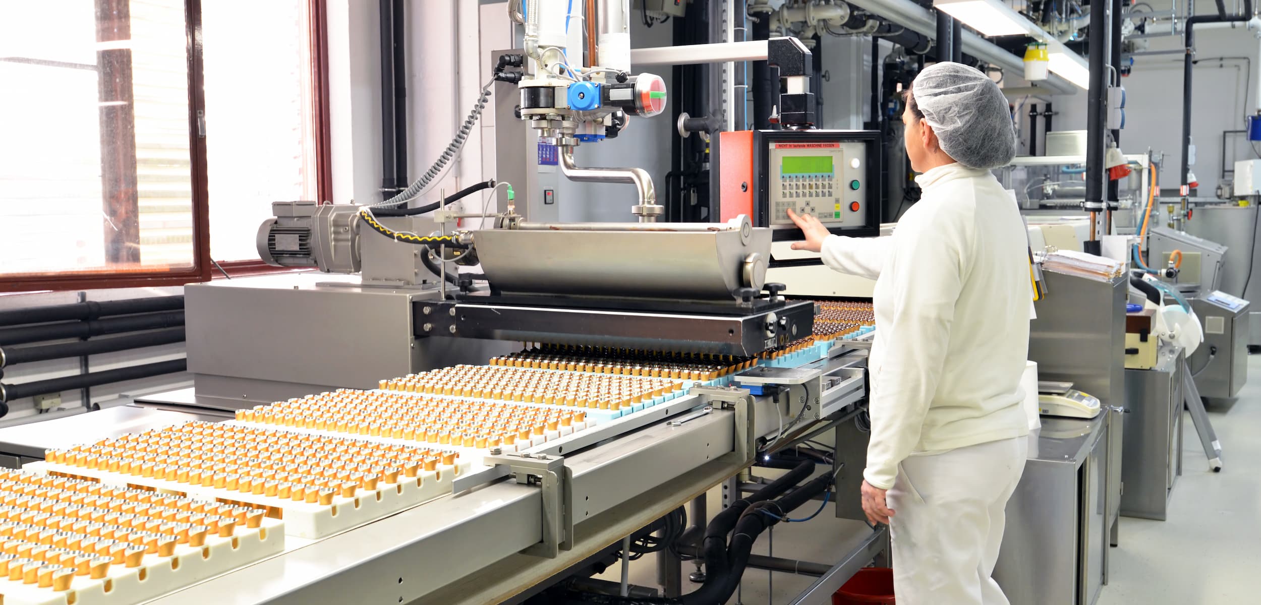 Person in a cleanroom observing a conveyor belt with products in an industrial setting