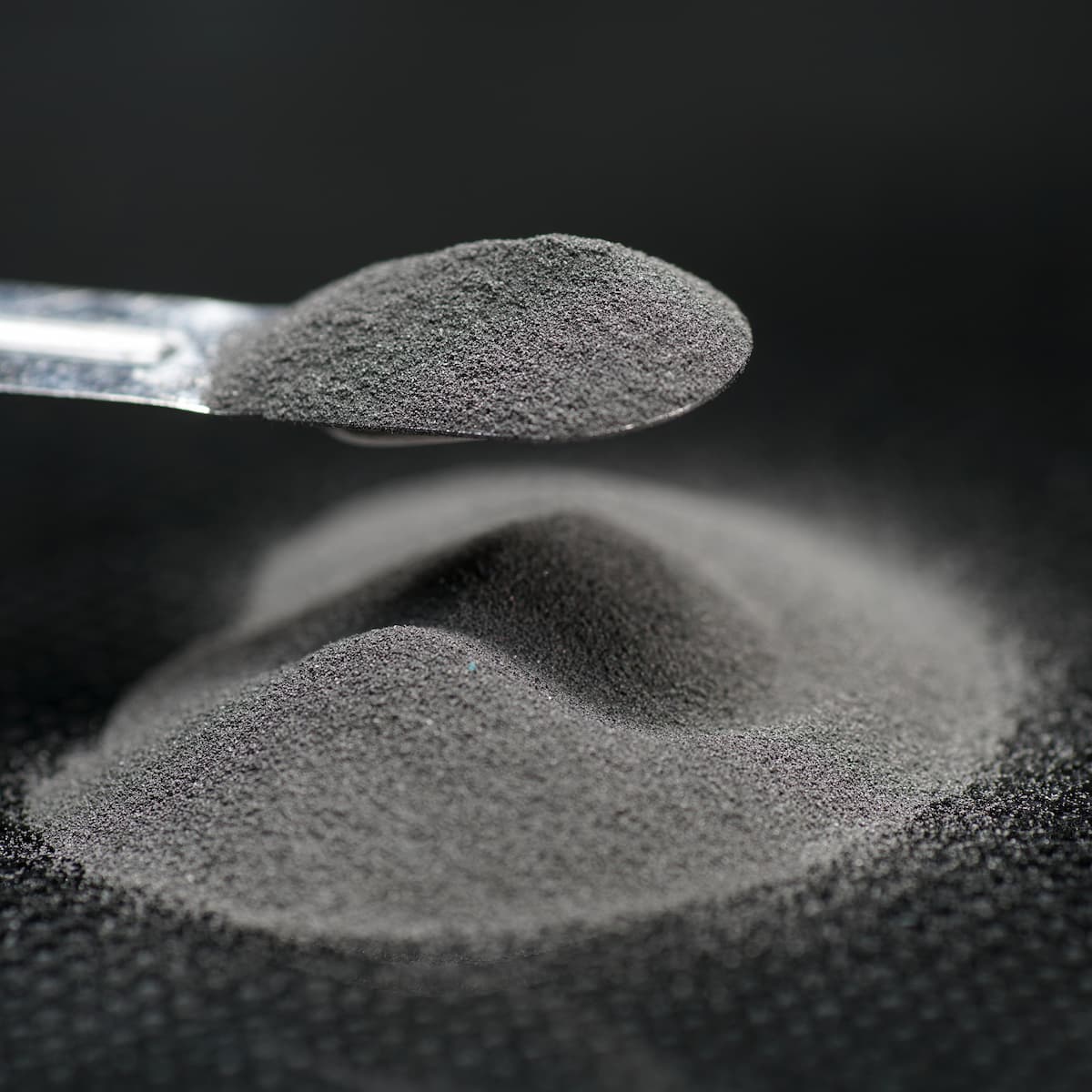 Spoonful of black powder over a pile of black powder on a dark background