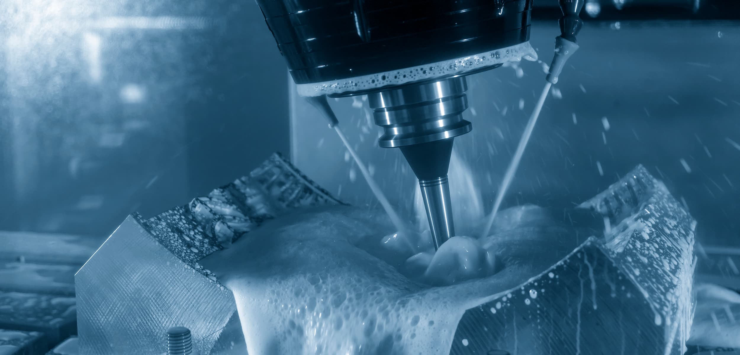 CNC milling machine cutting a piece of metal with a blue filter.