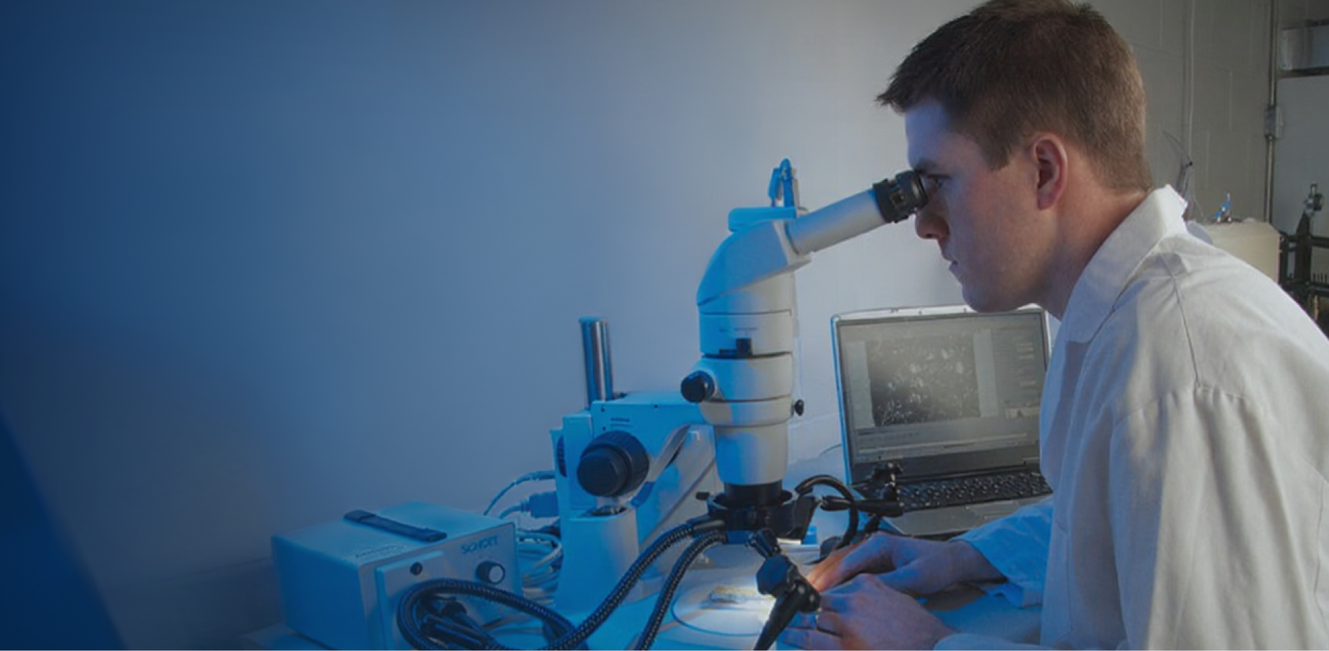 man at desk looking through microscope