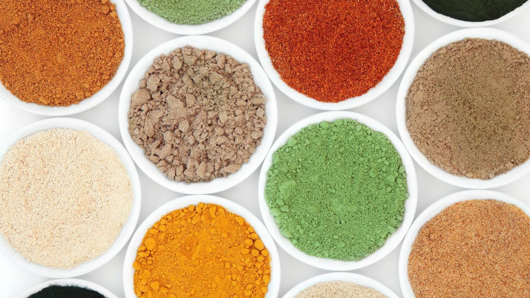 Assorted spices in small white bowls on a white background
